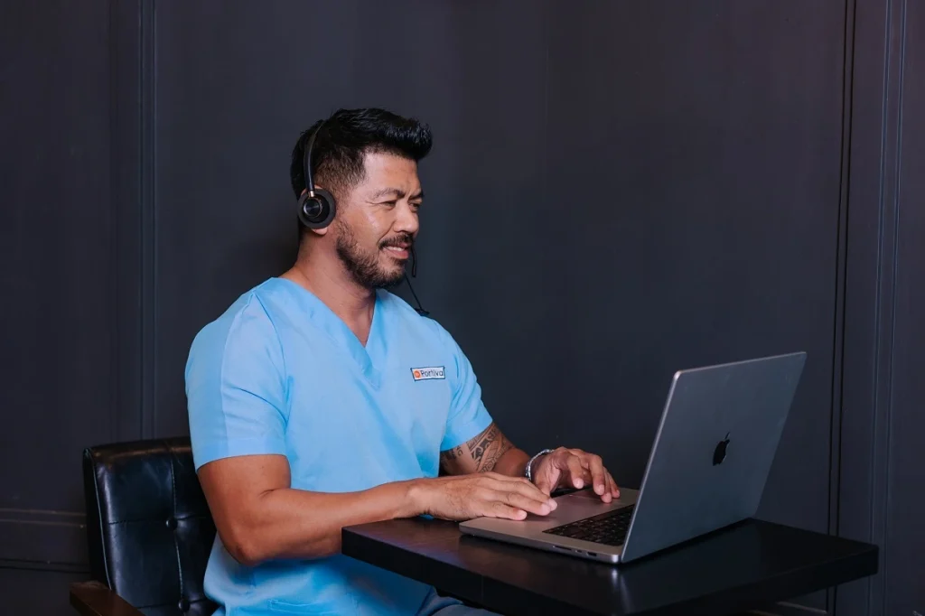 Medical answering services professional in scrubs wearing a headset while assisting patients from a laptop