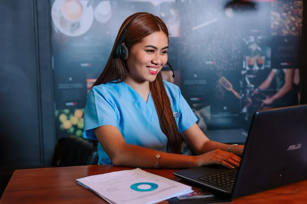 Medical coding services support professional in blue scrubs wearing a headset while working on a laptop