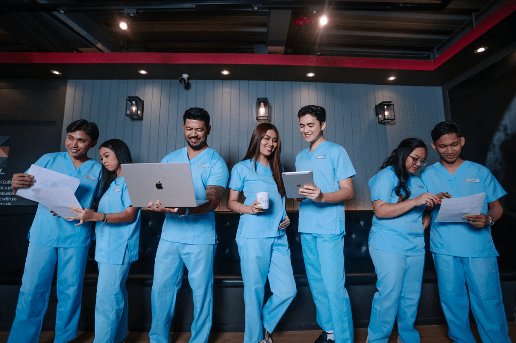 portiva medical virtual assistant team members in blue scrubs working together with laptops, tablets, and documents in an office setting