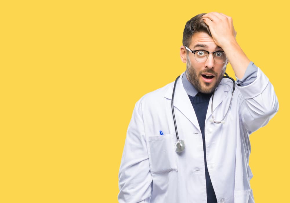 Young handsome doctor man over isolated background surprised with hand on head for mistake