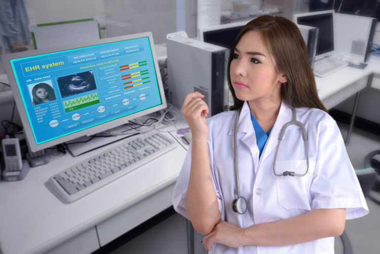 Female doctor stand in front of computer while showing electronic health record on monitor.