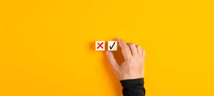 Right and wrong icons on wooden cubes with male hand choosing the right icon on yellow background. Approving, voting or right decision concept