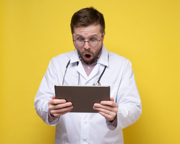 Frightened, shocked doctor looks at a tablet with an open mouth and big eyes. Yellow background
