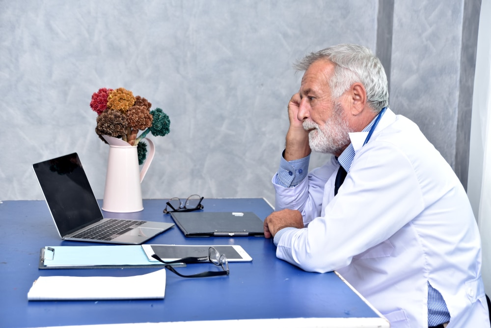 Handsome senior medical doctor in white coat is thinking and looking seriously at doctor's office