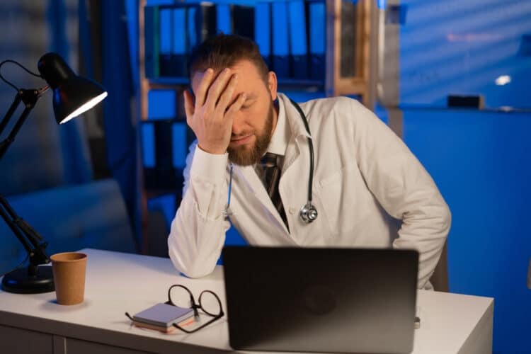 Male tired doctor with migraine overworked, overstressed working at night. sad unhappy health care professional with headache stressed sleepy. Copy space