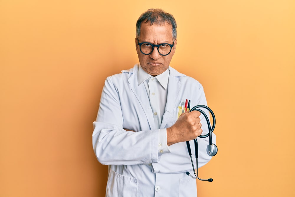 Middle age indian man wearing doctor coat holding stethoscope skeptic and nervous, frowning upset because of problem