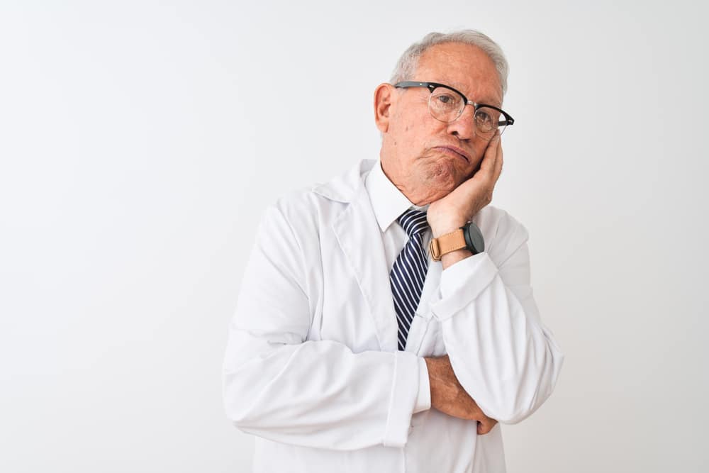 Senior grey-haired scientist man wearing coat standing over isolated white background thinking looking tired and bored with depression problems with crossed arms