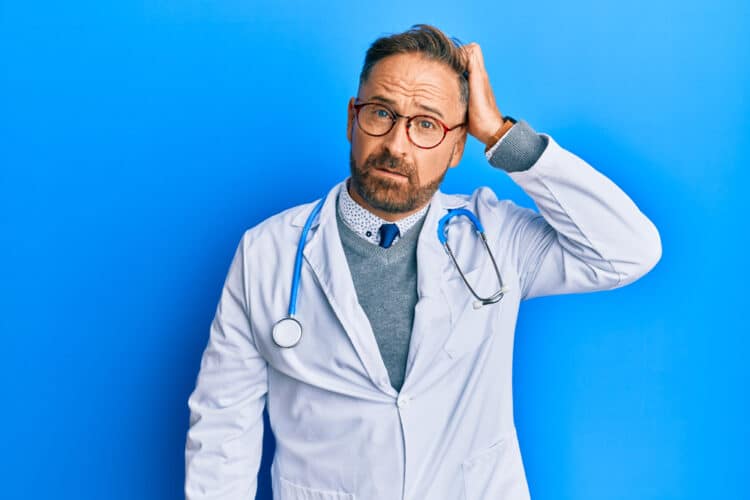 Handsome middle age man wearing doctor uniform and stethoscope confuse and wonder about question