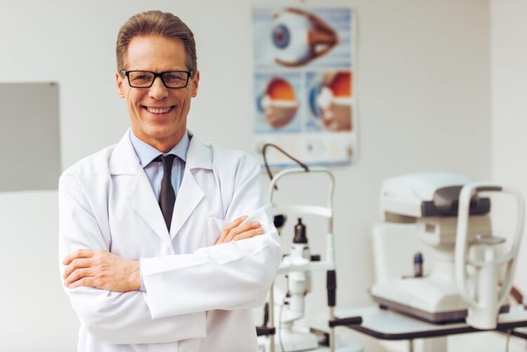 Handsome middle aged ophthalmologist looking at camera and smiling while standing in his office