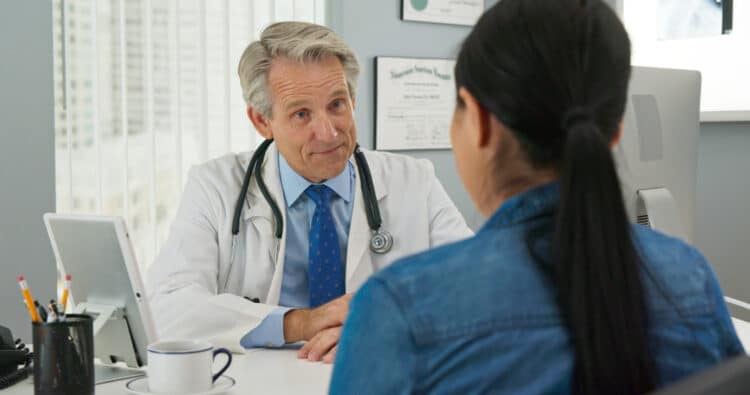 Mature Caucasian male doctor in his office listening to new patient and smiling