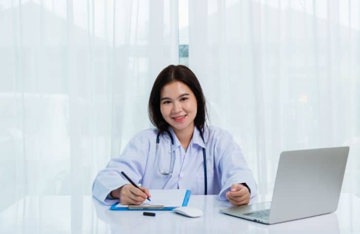 optimizing prior authorization smiling doctor using a laptop and writing something