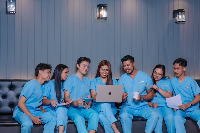A diverse team in light blue scrubs works together, sharing screens and documents.