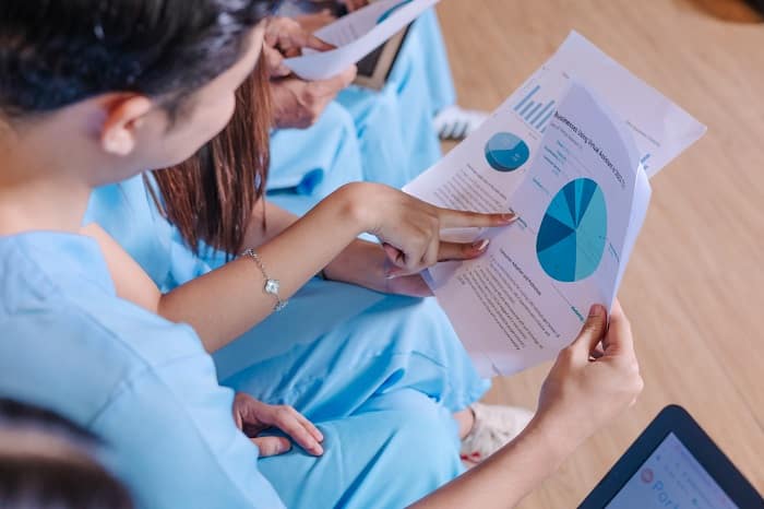 A person in blue medical scrubs points to a pie chart on a business document during a meeting