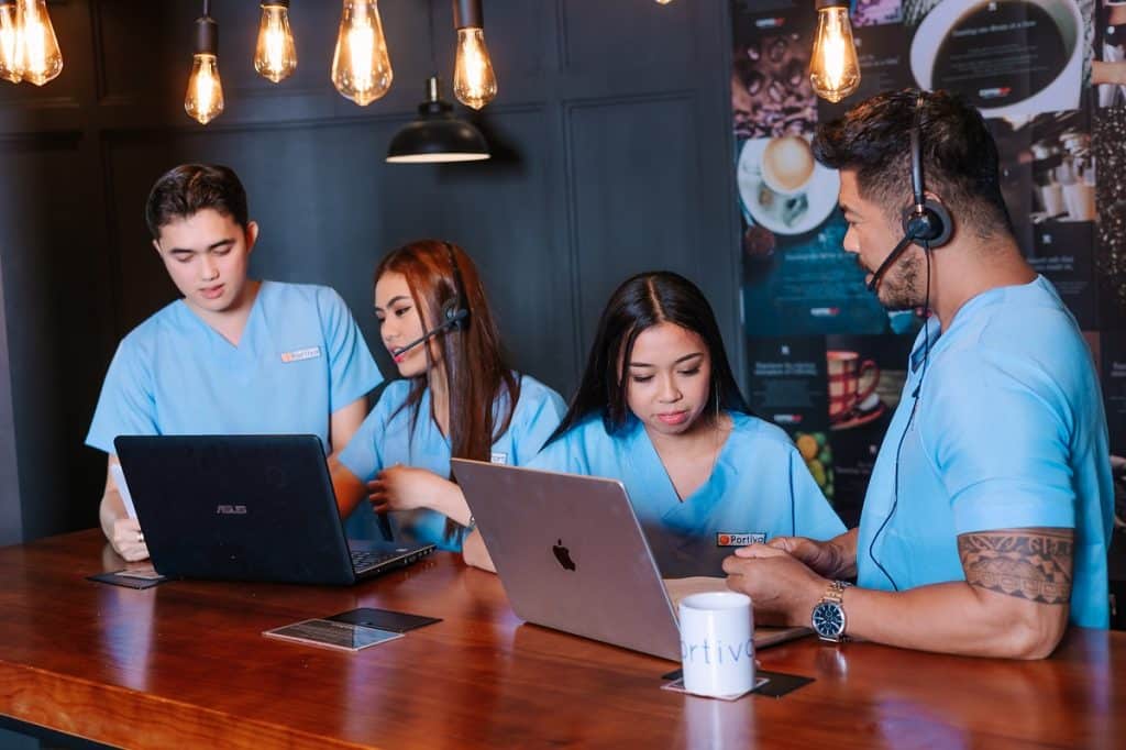 A team of healthcare professionals in blue scrubs collaborates with laptops and headsets, showcasing revenue cycle management services for small practices in a modern office environment.