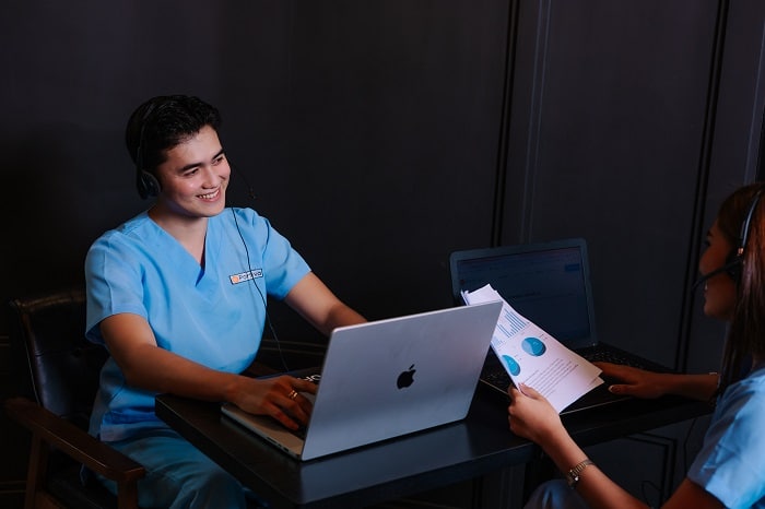 Benefit verification authorization services with two people in medical scrubs and headsets collaborate on laptops.