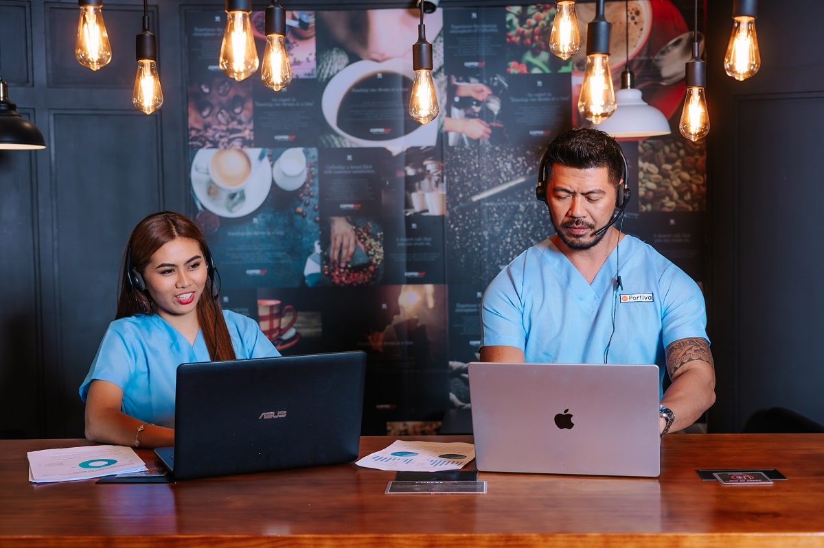 Medical coding audit services with two professionals in scrubs with headsets work on laptops.