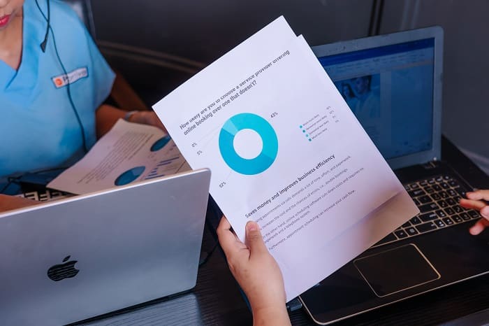 staff reviewing a document with a pie chart showing business efficiency data over two laptops.