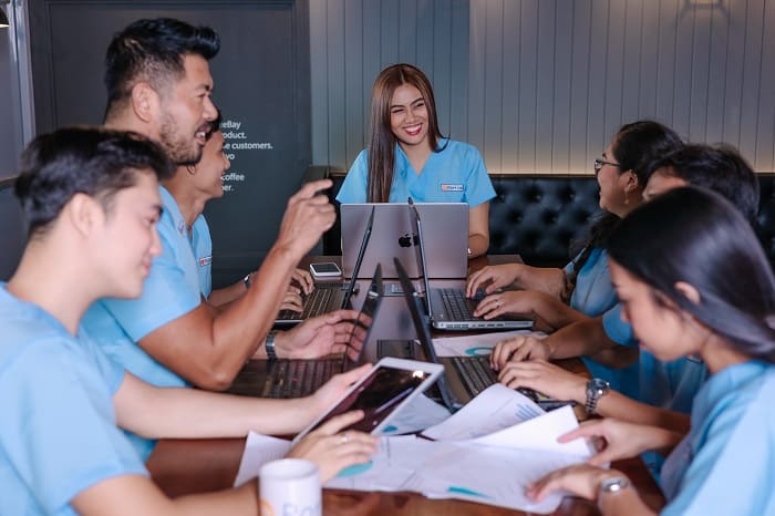 A team of seven professionals in light blue uniforms are gathered around a conference table