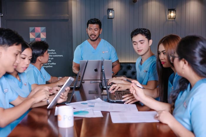 best remote medical scribe companies with seven medical staff in scrubs collaborate on laptops at a dark wooden conference table.