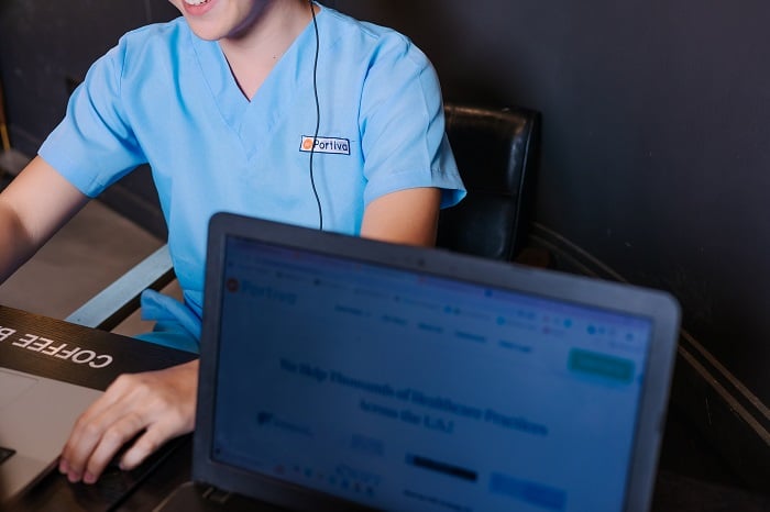 close-up of a person in scrubs with a headset and laptop, smiling