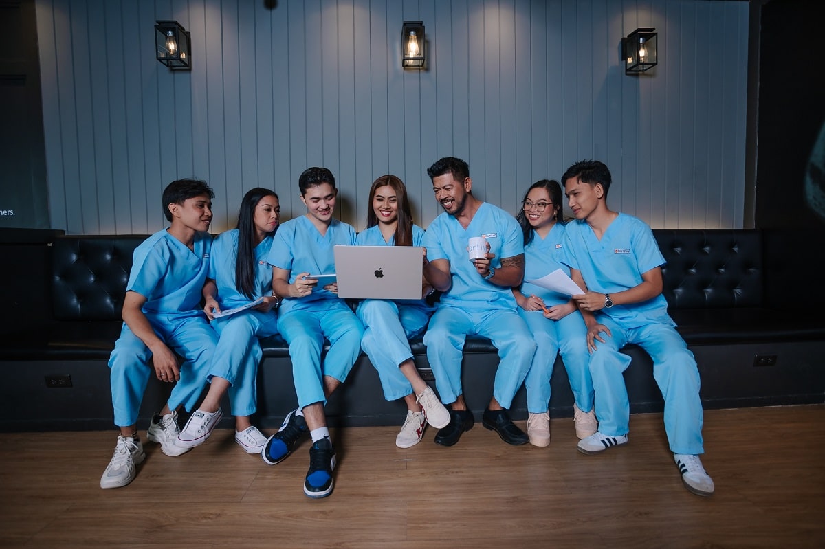 do you want to become a virtual assistant find your niche wih six medical professionals in scrubs gathered around a laptop.