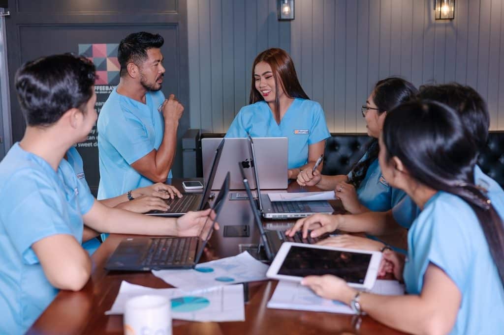 Prior authorization follow up high intent patients collaborating in a team meeting with laptops and tablets to coordinate workflows